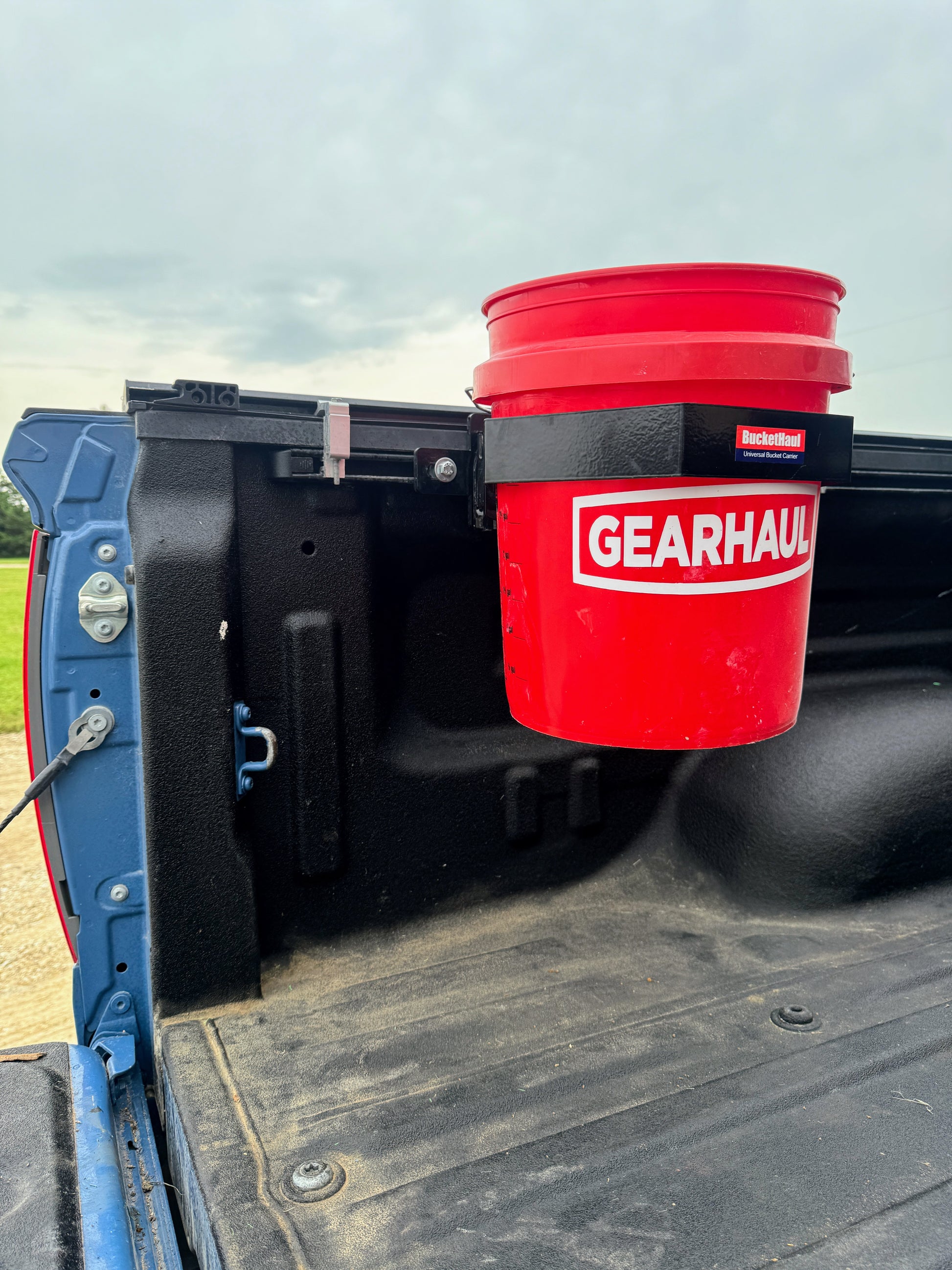Red GEARHAUL bucket in a truck bed with a cloudy sky background